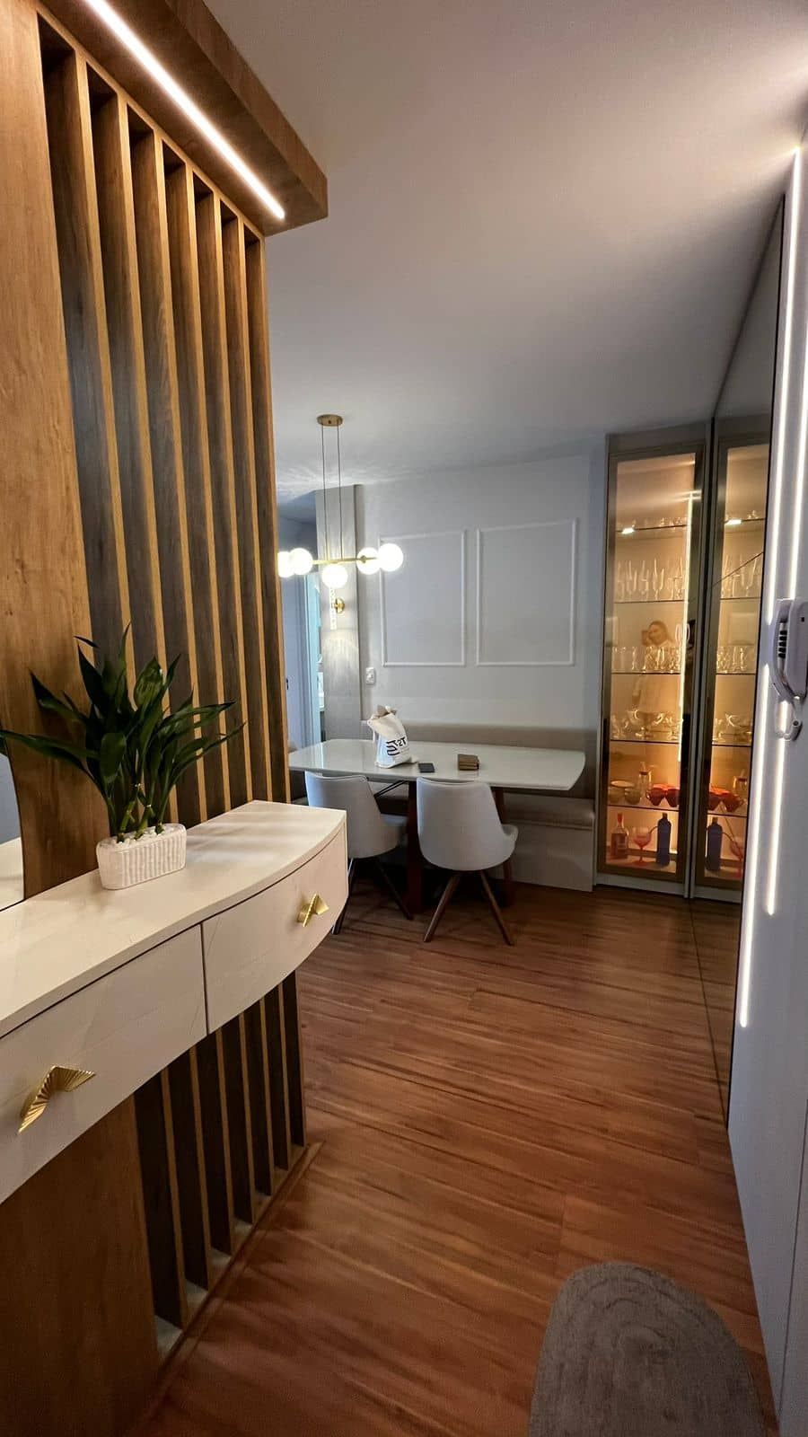 Hall com ripado amadeirado e aparador curvo, com a sala de jantar ao fundo