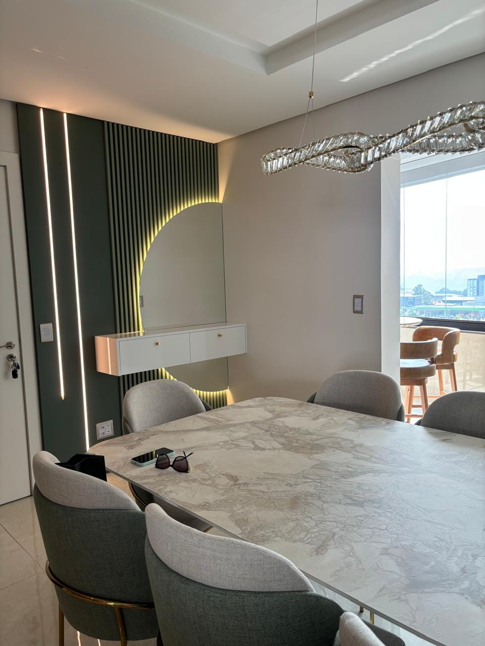 Sala de jantar com mesa marmorizada, ripado verde e espelho em meia-lua