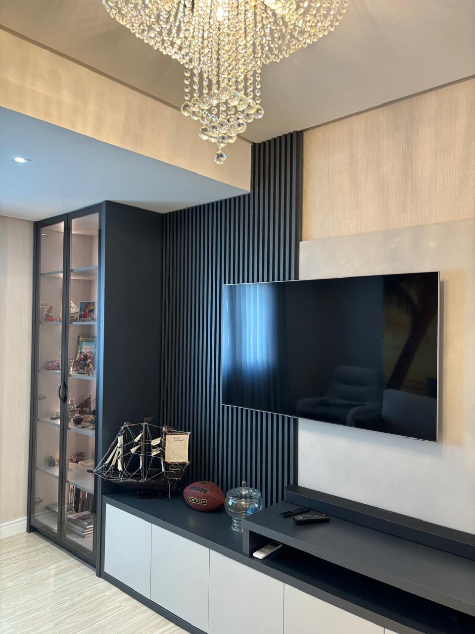 Sala com ripado preto, TV e lustre de cristal