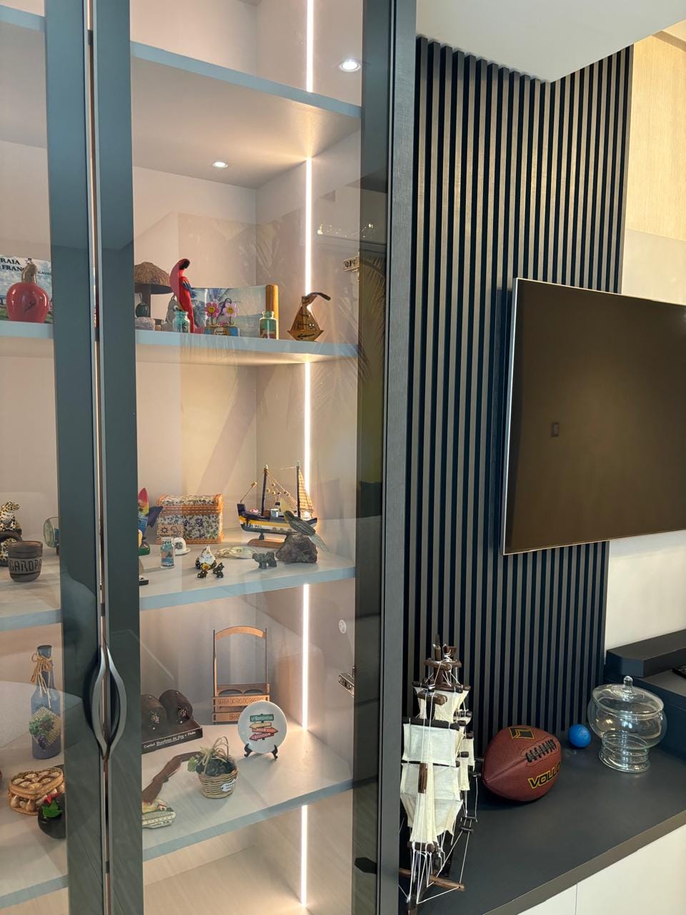 Vitrine iluminada com objetos de coleção ao lado da TV
