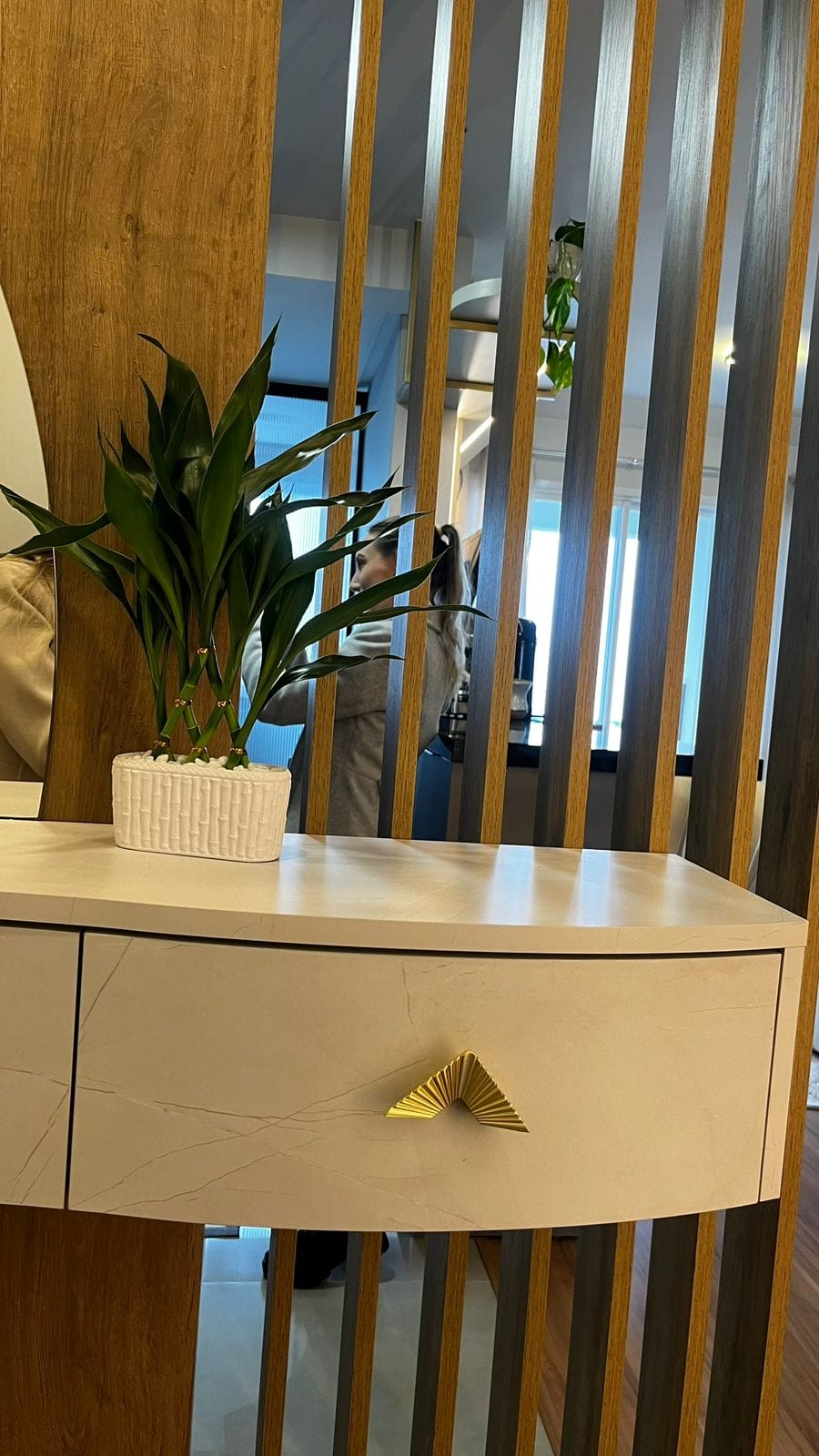 Detalhe do aparador curvo com puxador dourado diante do ripado