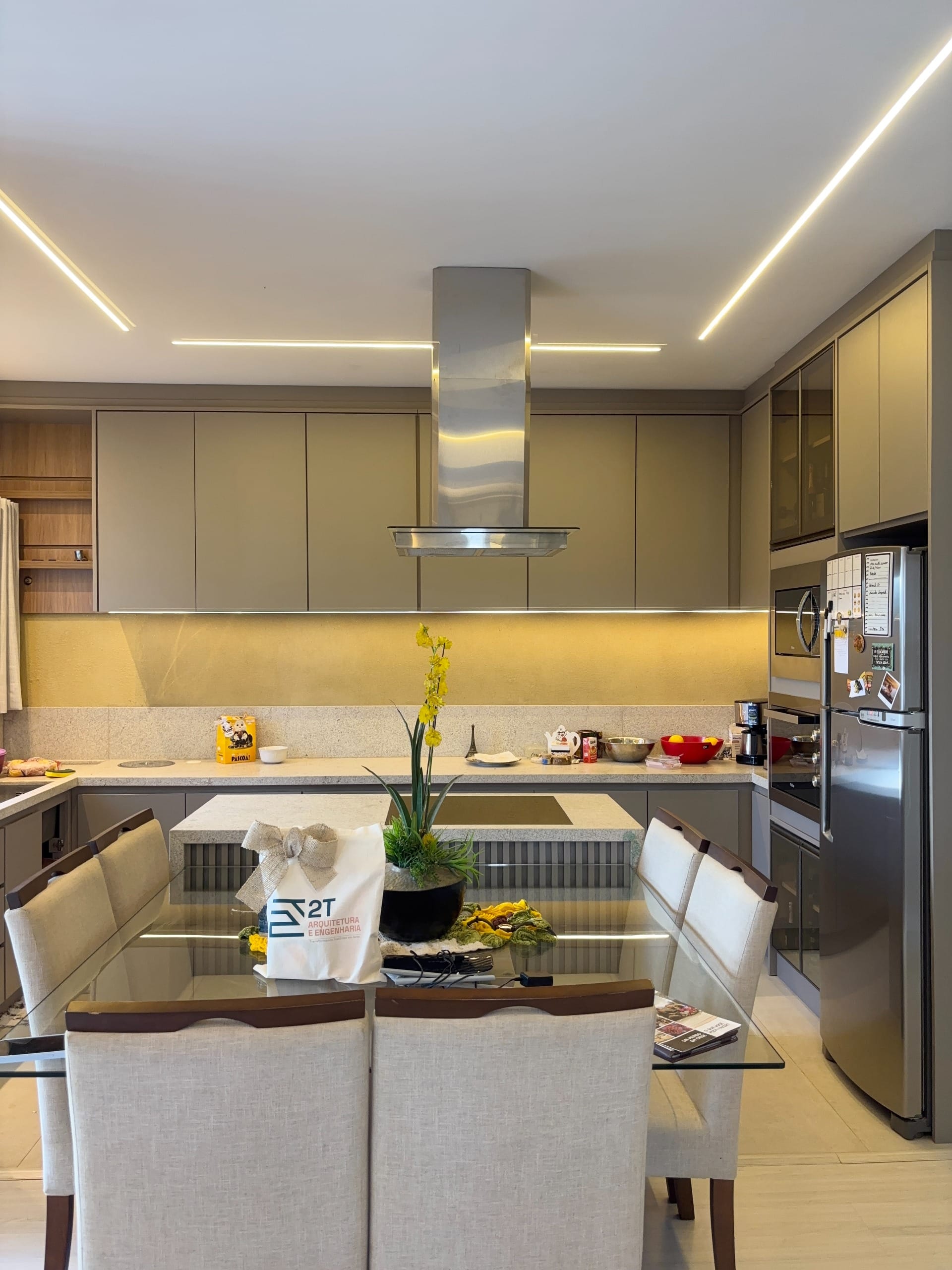 Cozinha com coifa em inox, mesa de vidro e cadeiras brancas