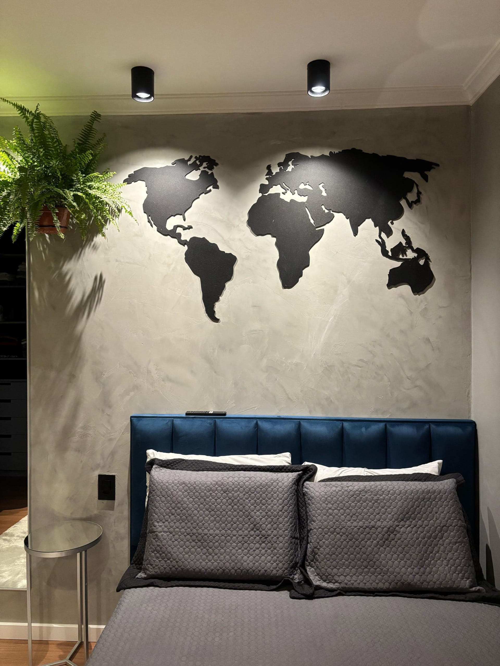 Quarto com mapa-múndi preto na parede de cimento queimado e cabeceira azul