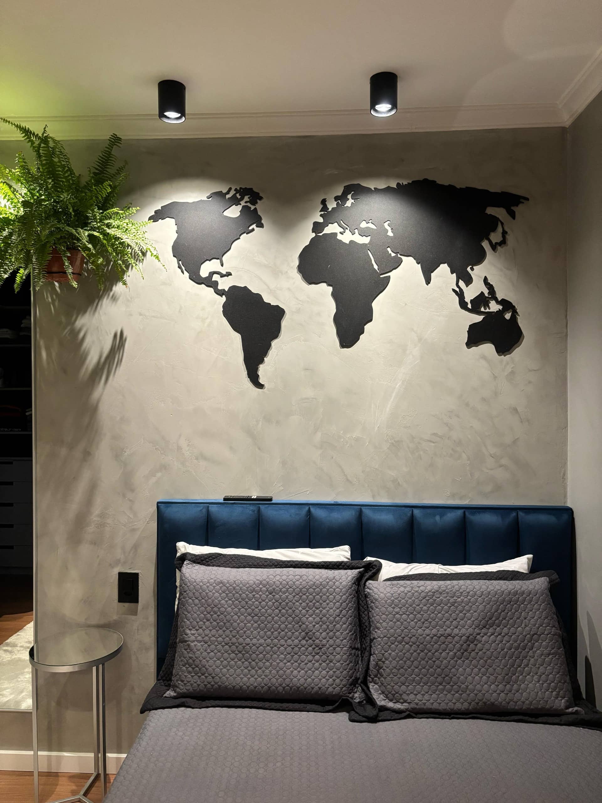 Quarto com mapa-múndi preto na parede de cimento queimado e cabeceira azul